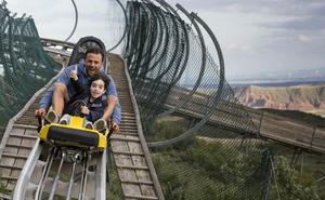 Un adulto y un niño se deslizan por la pista de bobsleigh que atraviesa el parque./